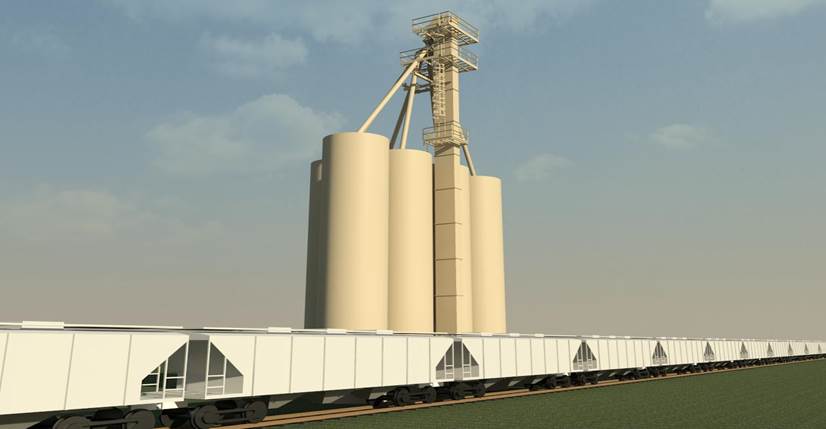 Bucket elevator leg rising beside grain storage silos above a line of covered hopper railcars