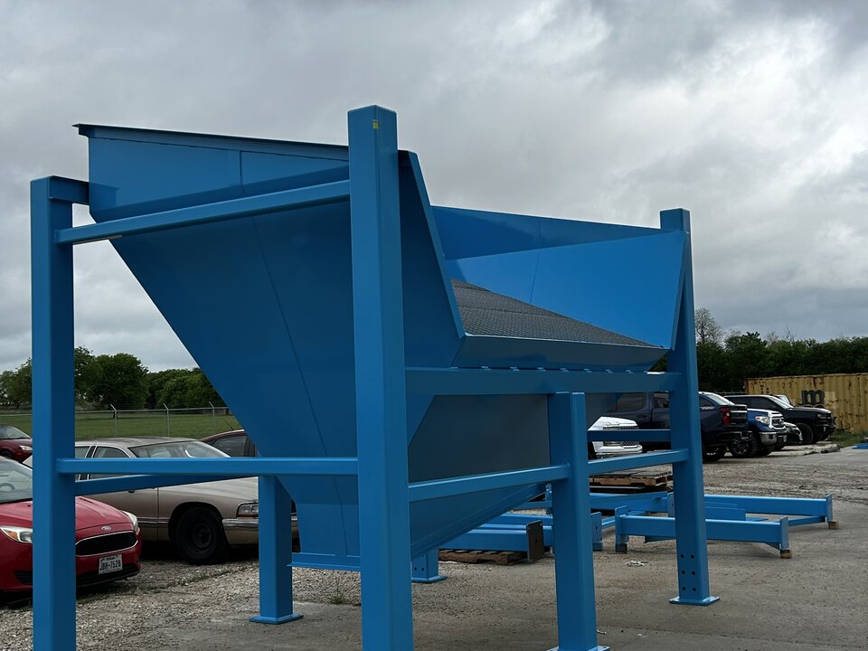Orthman hopper on a four-leg steel support stand, finished in blue and staged outdoors